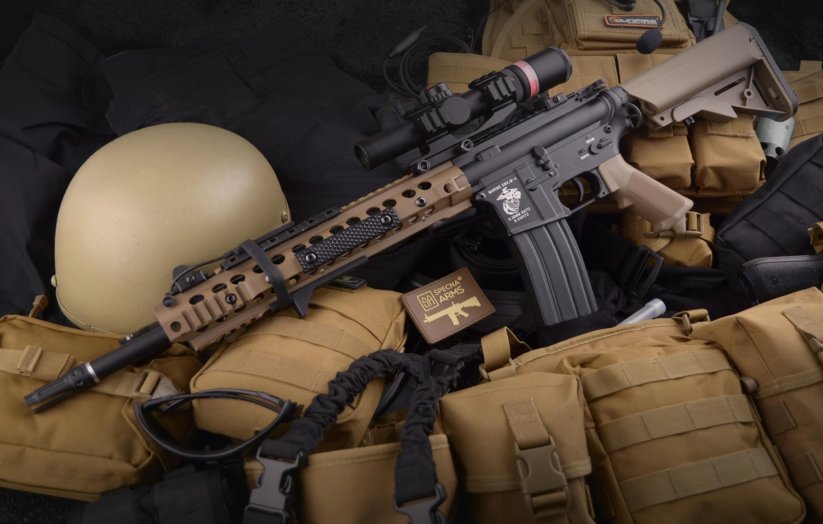 Rifle de airsoft Specna Arms M4 customizado em tons de preto e coyote sobre colete tático, capacete e equipamentos balísticos